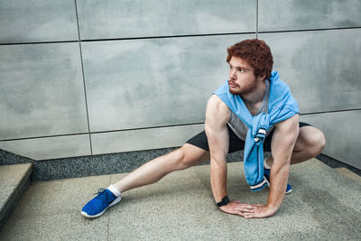 Young man looking away while sitting on wall