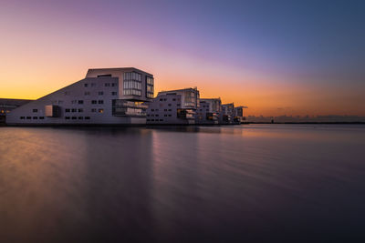 Buildings by sea against sky during sunset