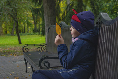 Rear view of boy sitting on bench against trees