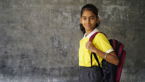 Smiling indian rural school girl with backpack looking at camera.