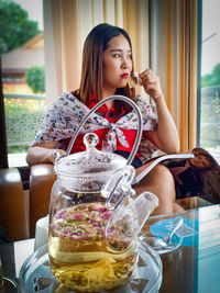 Thoughtful mid adult woman drinking herbal tea while looking away at home