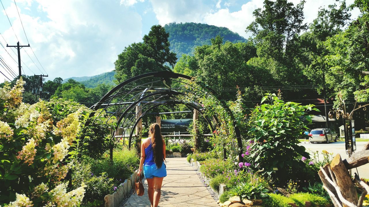 REAR VIEW OF WOMAN WALKING ON PLANTS AGAINST BUILDING