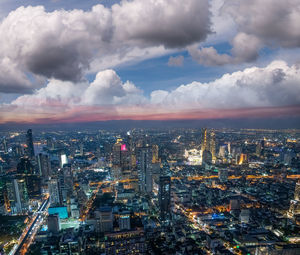 Aerial view of illuminated city against cloudy sky