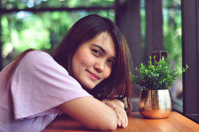 Portrait of beautiful woman sitting by potted plant on table