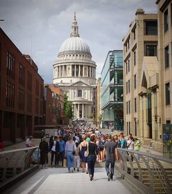 People walking on street amidst buildings in city against sky