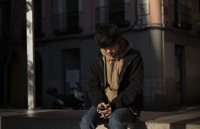 Asian teenage boy looking at mobile phone on street. madrid. spain