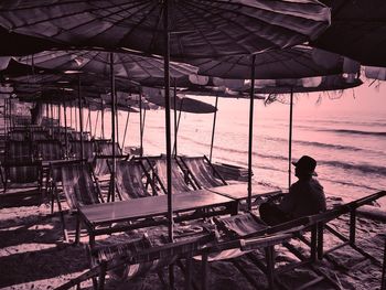 Rear view of man sitting on railing at beach