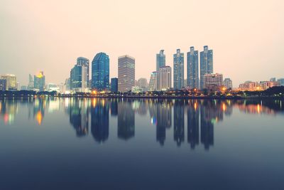 Reflection of illuminated buildings in city against clear sky