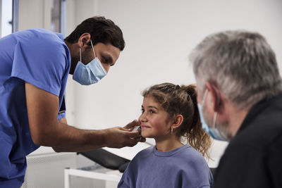 Male doctor examining girl patient's ear during appointment