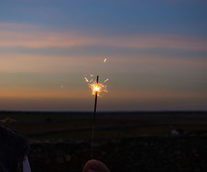 Person holding umbrella against sky during sunset