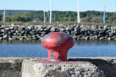 Close-up of red metallic bollard on concrete retaining wall by river canal