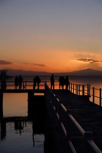 Silhouette people on pier over sea against sky during sunset