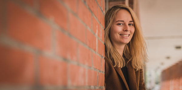 Portrait of young woman standing by brick wall