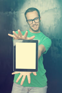 Portrait of young man showing digital tablet while standing against old wall