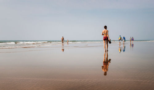 Rear view of woman walking on shore at beach against sky