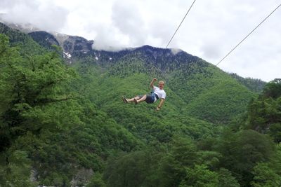 Rear view of man and rope on mountain against trees