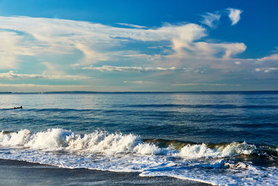 Scenic view of sea with crashing waves against cloud and sky