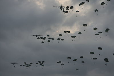 Low angle view of paratroopers parachuting from aircraft against cloudy sky