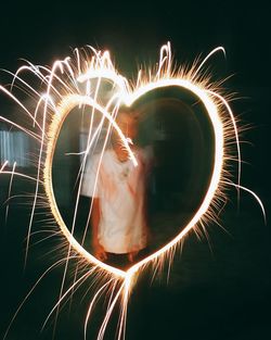 Man forming heart shape with sparkler at night