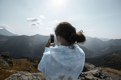 Rear view of man photographing on mountain against sky
