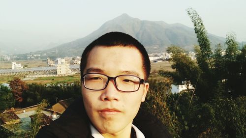 Close-up of young man in eyeglasses standing against mountain