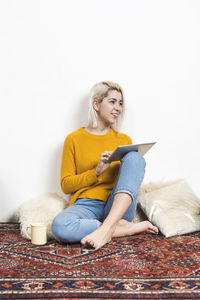 Portrait of young woman using laptop while sitting on hardwood floor against white background