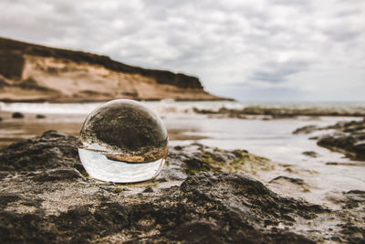 Close-up of crystal ball on rock by sea against sky