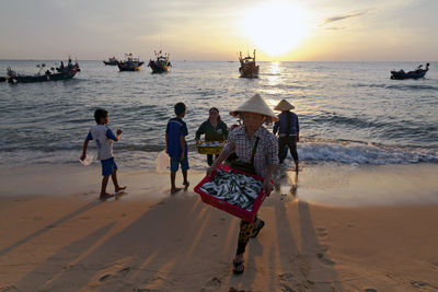 People on beach against sky during sunset