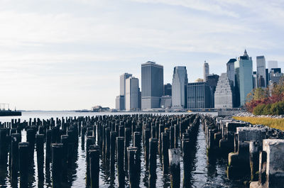 Poles in river with buildings against sky