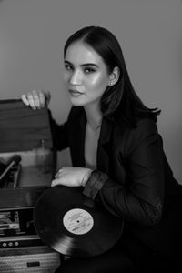 Portrait of woman sitting by vintage record player against wall