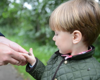 Cropped image of hand person holding hand of boy with frog against plants
