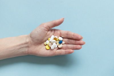 Cropped hand of woman holding pills against blue background