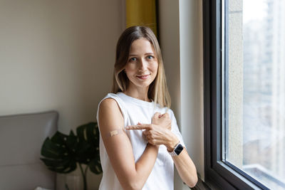 Portrait of smiling woman standing against window at home