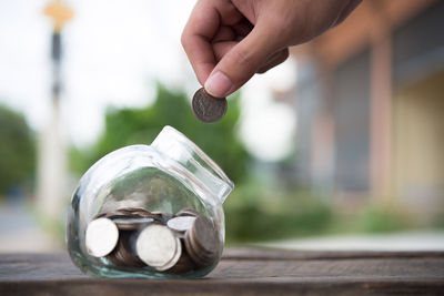 Close-up of person putting coin in jar on table