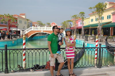 Full length of family standing on footbridge over lake against sky