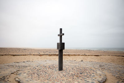 Religious cross at beach against sky