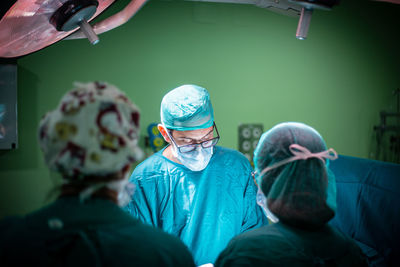 Male doctor in glasses and uniform performing surgery on patient with help of assistants in modern operating theater of hospital