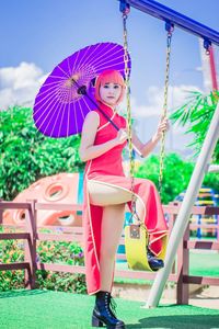 Portrait of young woman with dyed hair holding umbrella while standing on swing