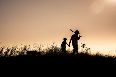 Silhouette father and son walking on field against sky during sunset