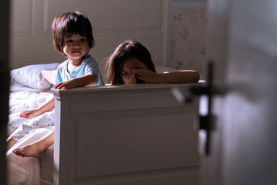 High angle view of siblings sitting on bed