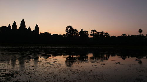 Silhouette trees by lake against sky during sunset