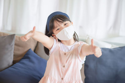 Portrait of girl wearing mask gesturing while sitting on sofa