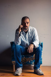 Portrait of young man sitting against wall