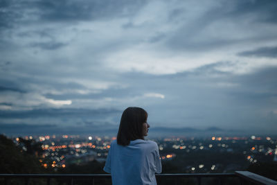 Rear view of woman looking at cityscape against sky