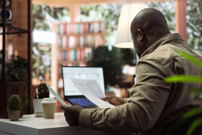 Rear view of man using digital tablet while sitting in library