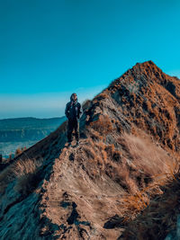 Man standing on rock against blue sky