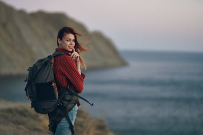 Young woman looking away while standing in sea against sky