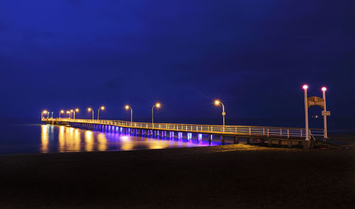 Illuminated bridge over sea against sky at night