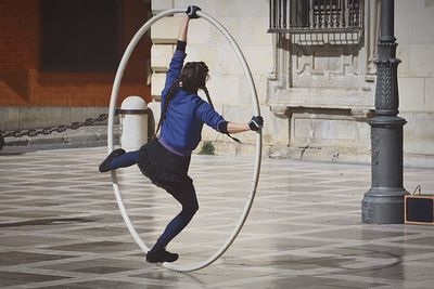 Rear view of woman performing acrobat with large ring on street