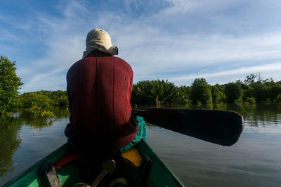 Rear view of man on boat in lake against sky